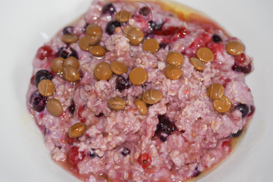 A Bowful of Pink Porridge with Mixed Berries, Chocolate Drips and Honey